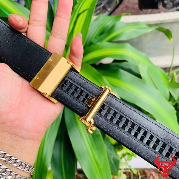 Hình ảnh thắt lưng da cá sấu TSK103, khóa thép mạ vàng, cầm trên tay giữa lá xanh và nền gỗ.