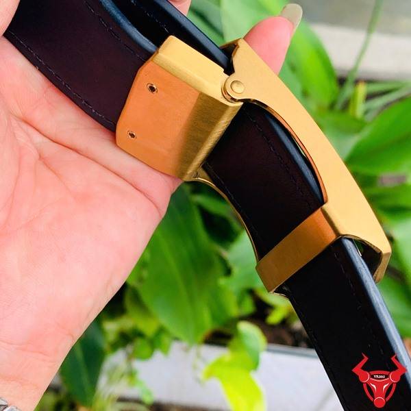 Hình ảnh thắt lưng da cá sấu xanh patina TSK33, khóa vàng, cầm trên tay giữa lá xanh và nền sáng.