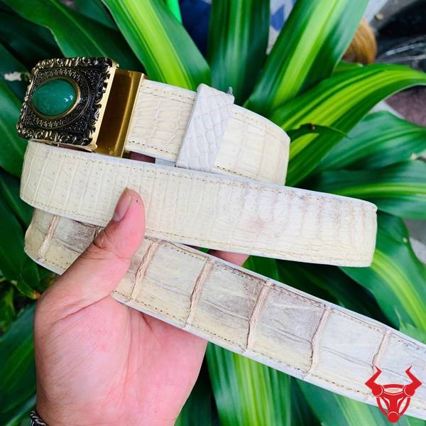 Hình ảnh thắt lưng da cá sấu bạch tạng TSK95, mặt khóa đồng nguyên chất, cầm trên tay với lá xanh.