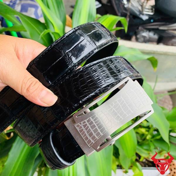 Hình ảnh thắt lưng da cá sấu TSK32, khóa lăn inox họa tiết cá sấu, cầm trên tay với lá xanh.