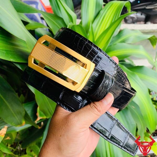 Hình ảnh thắt lưng da cá sấu TSK33, khóa tỳ thép vàng, cầm trên tay giữa lá xanh.