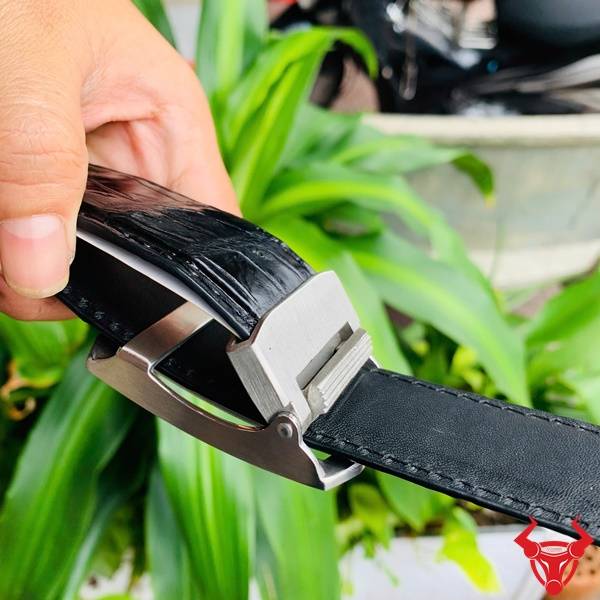 Hình ảnh dây lưng da cá sấu TSK33, khóa tỳ thép mạ bạc, cầm tay giữa lá xanh.