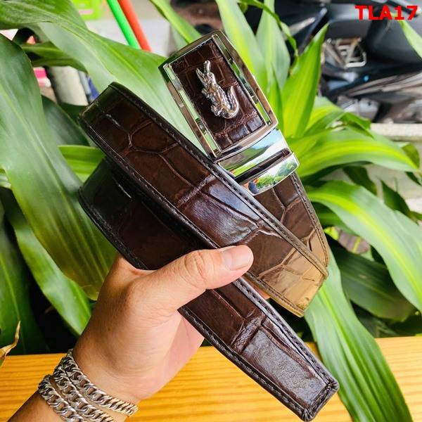 Hình ảnh thắt lưng da cá sấu nâu đất FBA9B2, viền bọc sang trọng, khóa kim loại mạ bạc, cầm trên tay giữa cảnh lá xanh.
