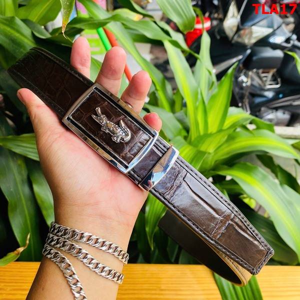 Hình ảnh thắt lưng da cá sấu nâu đất FBA9B2, viền bọc cao cấp, khóa mạ bạc, được cầm trên tay với nền lá xanh.