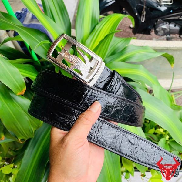 Hình ảnh thắt lưng da cá sấu TSK73, ray trượt sang trọng, mặt khóa inox khắc logo, cầm trên tay với lá xanh.