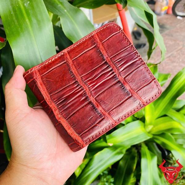 Hình ảnh ví da cá sấu nâu đỏ VBAA8, phong cách độc lạ, giữa cảnh cây xanh.
