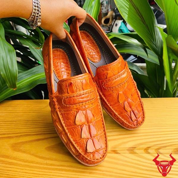 Hình giày tây GCA2 da cá sấu gai đuôi màu vàng cam trên chân, nền lá, cao cấp đẳng cấp quý ông.