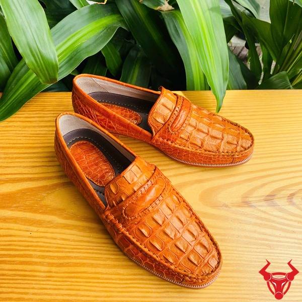 Hình đôi giày tây GCA1 da gai lưng cá sấu màu vàng cam cầm tay, nền lá, cao cấp đẳng cấp quý ông.