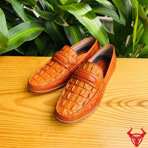 Hình đôi giày tây GCA1 da gai lưng cá sấu màu vàng cam cầm tay, nền lá xanh, cao cấp đẳng cấp quý ông.