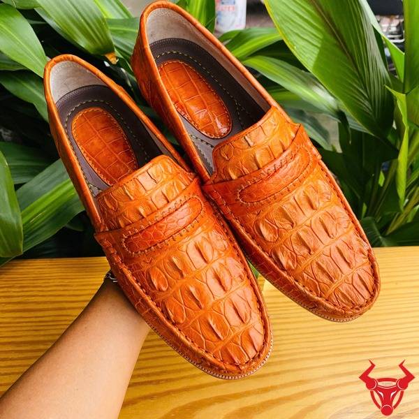 Hình giày lười GCA1 da cá sấu màu vàng cam trên bàn, nền lá, cao cấp đẳng cấp quý ông.