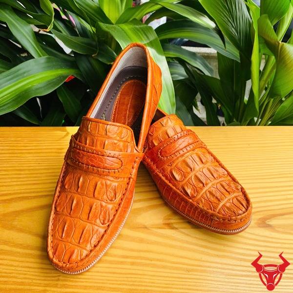 Hình đôi giày lười GCA1 da cá sấu màu vàng cam trên bàn, nền lá, cao cấp đẳng cấp quý ông.