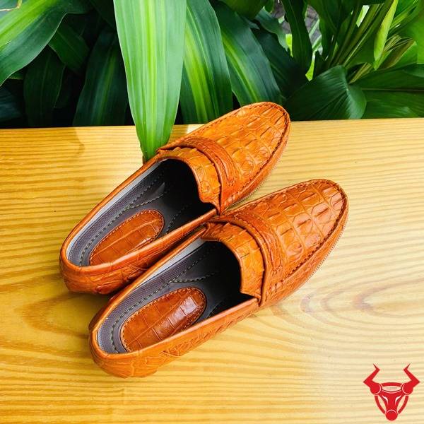 Hình đôi giày lười GCA1 da cá sấu màu vàng cam trên bàn, nền lá xanh, cao cấp đẳng cấp quý ông.