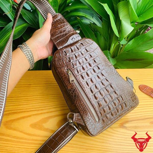 Ảnh túi đeo chéo TTL05 da cá sấu màu nâu đất, nền lá xanh, cao cấp phong cách đẳng cấp.