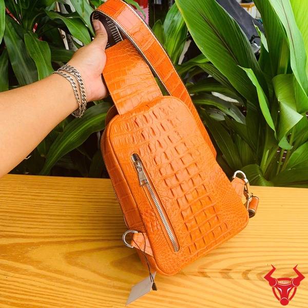 Ảnh túi đeo chéo TTL05 da cá sấu gù màu vàng cam, nền lá, thể hiện cao cấp phong cách.