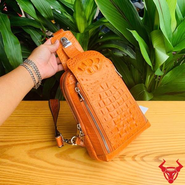 Hình túi TTL05 da cá sấu gù màu vàng cam trên bàn, nền lá, cao cấp phong cách.