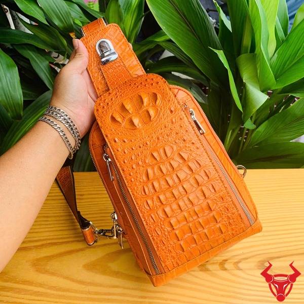 Ảnh túi đeo chéo TTL05 da cá sấu gù màu vàng cam, nền lá xanh, cao cấp phong cách.