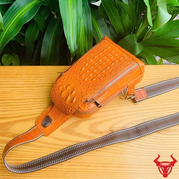 Ảnh túi TTL05 da cá sấu gù màu vàng cam trên bàn, nền lá, cao cấp phong cách.