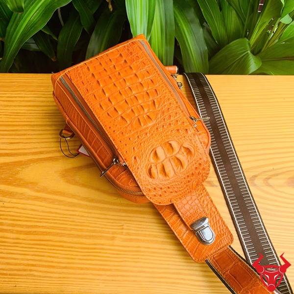 Hình túi đeo chéo TTL05 da cá sấu gù màu vàng cam, nền lá xanh, cao cấp phong cách.