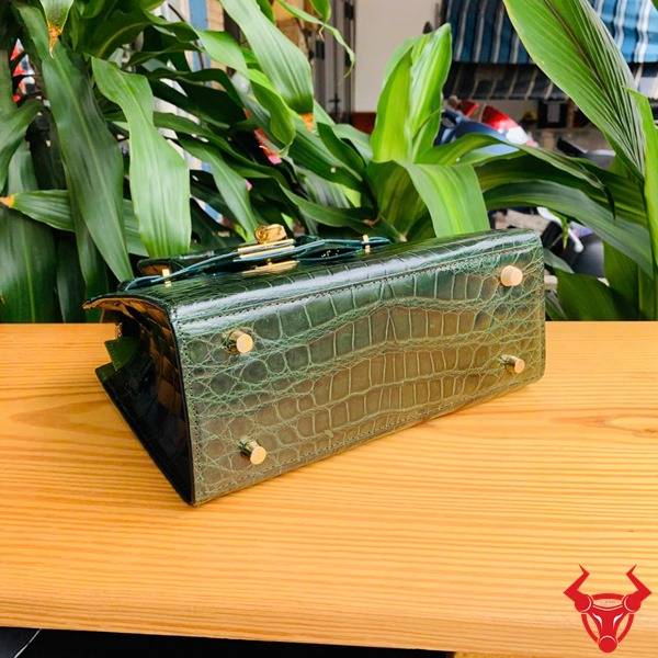 Hình túi xách TTL01 da cá sấu bóng kính cầm tay, nền lá xanh, thể hiện thời trang cao cấp sang chảnh quý phái.
