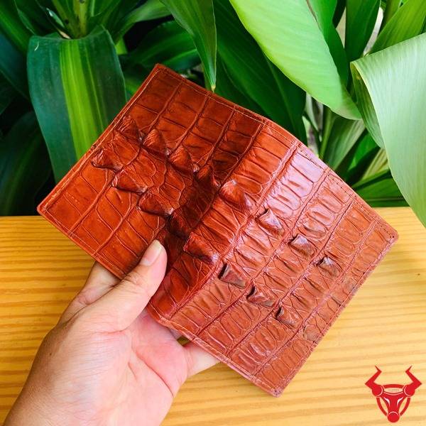 Ảnh ví đứng VJA2 da cá gai đuôi cá sấu màu nâu đỏ cầm tay, nền lá, thể hiện cao cấp sang trọng cá tính.
