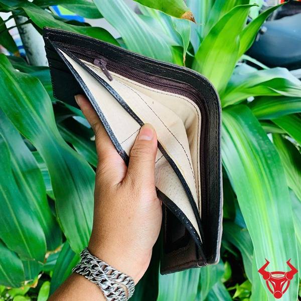 Ảnh hai ví VBA4 da cá sấu gù lớn màu nâu đất cầm tay, nền xanh, cao cấp cá tính ấn tượng.