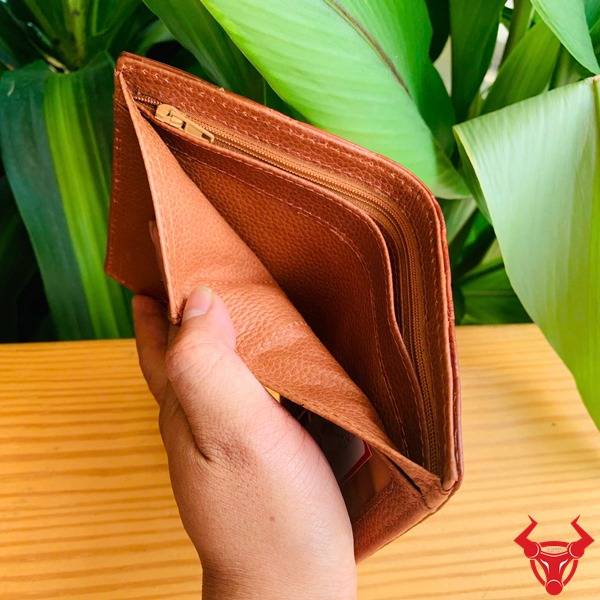 Hình ví form đứng VJA8 da cá sấu màu nâu đỏ sáng cầm tay, nền lá, thể hiện cao cấp sang trọng.
