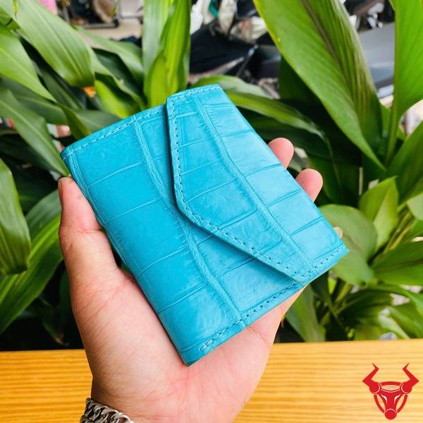 Ba chiếc ví mini da cá sấu xanh ngọc trong ảnh, cầm trên tay với nền lá cây, đại diện cho phong cách thời trang tinh tế.
