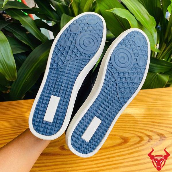 Ảnh giày thể thao da cá sấu đen GCS25, đặt trên bàn với nền lá xanh và thẻ logo.