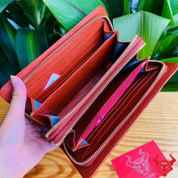 Ảnh chi tiết ví da cá sấu nâu đỏ với 2 khuôn thụt, đặt trên bàn với nền lá xanh.