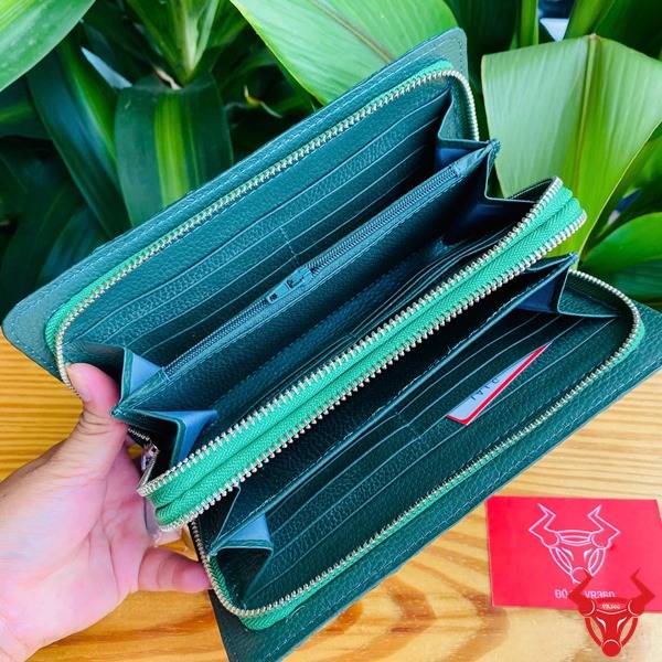Ảnh chi tiết ví da cá sấu xanh lá với 2 khuôn thụt, cầm tay trên nền gỗ và lá.