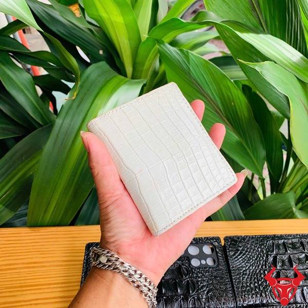 Ảnh sản phẩm ví da cá sấu trắng mộc form đứng, cầm tay với nền thực vật xanh.