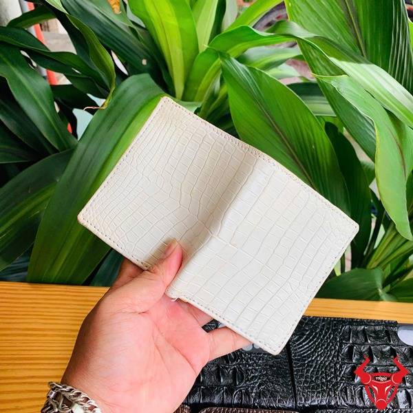 Bức ảnh ví mini da cá sấu trắng mộc được cầm trên tay, bên cạnh phụ kiện da đen.