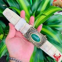 Hình ảnh thắt lưng da cá sấu bạch tạng TSK95 màu kem, mặt khóa đồng nguyên chất, cầm tay trên nền lá xanh.